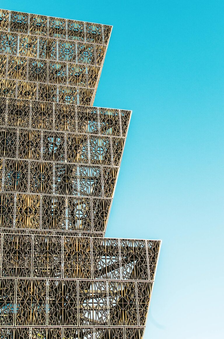 Close-up of a modern building facade with intricate lattice patterns against a clear blue sky.